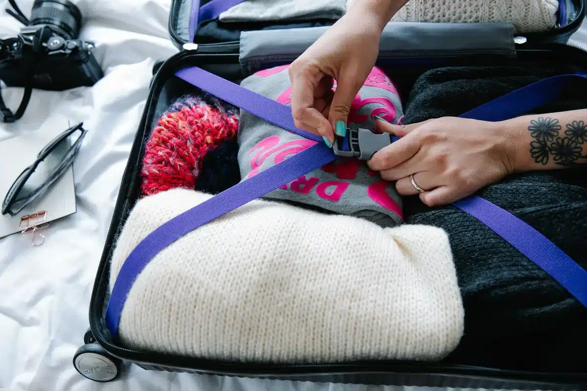 Valise ouverte avec vêtements pliés, passeport et accessoires de voyage organisés sur un lit