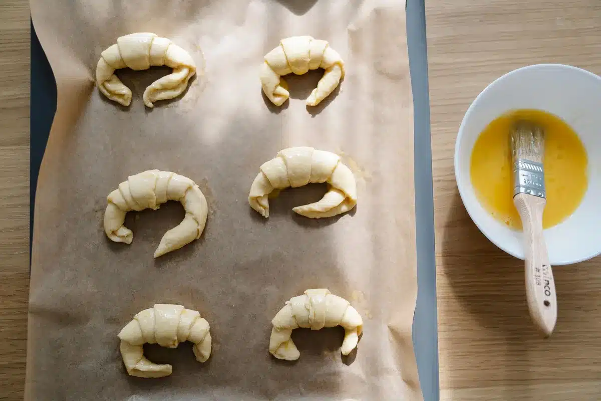 Mains façonnant une pâte feuilletée jaune avec couches de beurre visibles sur un plan de travail de cuisine