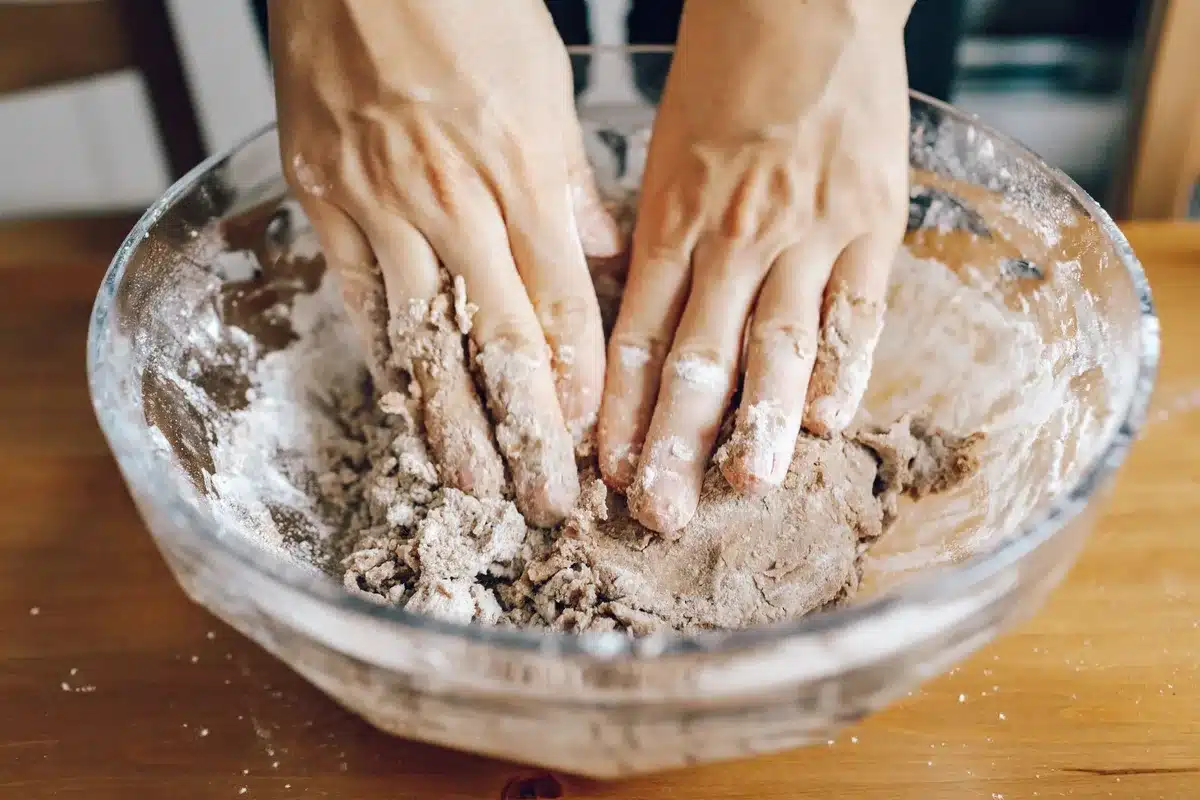 Mains pétrissant une pâte blanche homogène dans un saladier