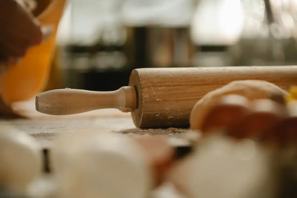 Mains roulant une pâte briochée garnie de pommes et de crème à la cannelle sur un plan de travail fariné