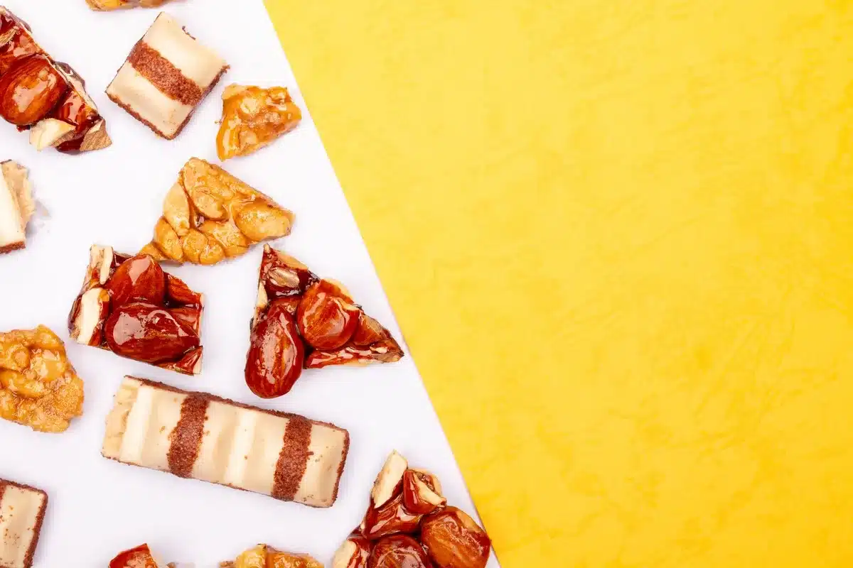 Main versant du caramel chaud sur un bloc de nougat tendre dans un cadre, avec des graines et noix caramélisées à proxim