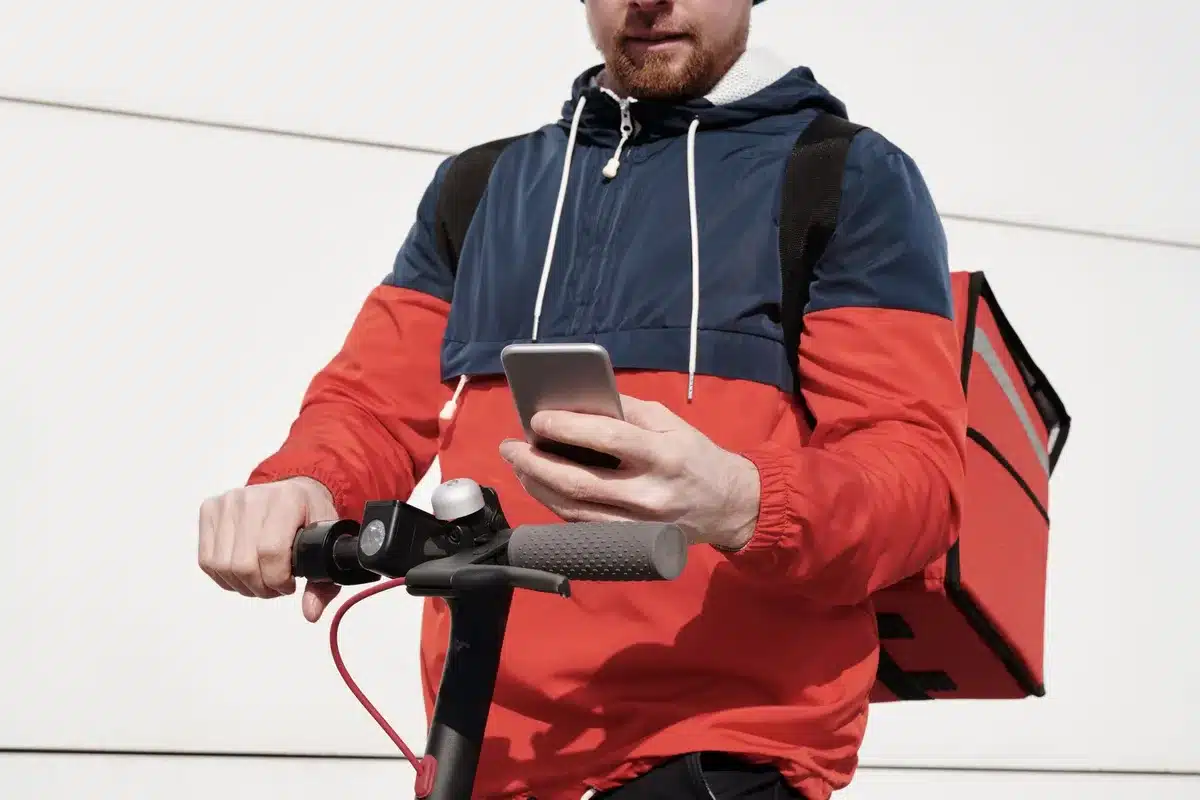 Livreur à scooter circulant en ville avec application mobile visible sur téléphone