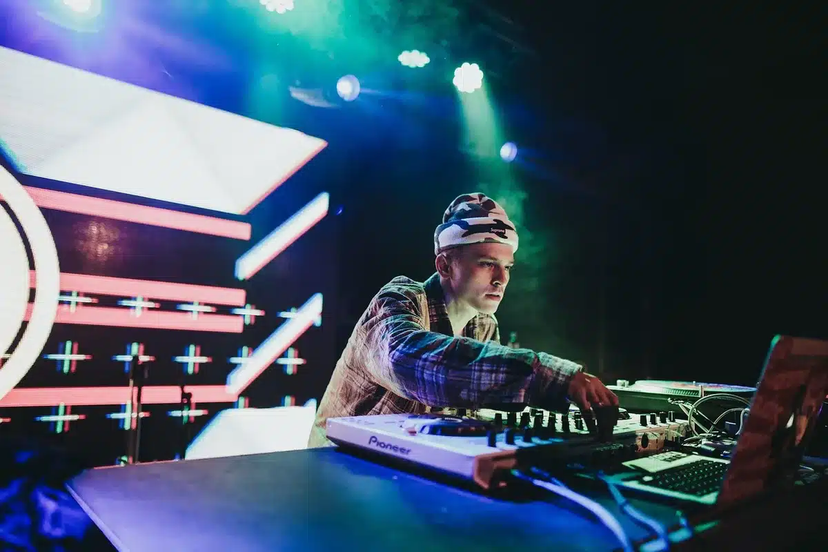 DJ en cabine jouant de la musique électro devant une foule dansante, avec jeux de lumière et écrans visuels